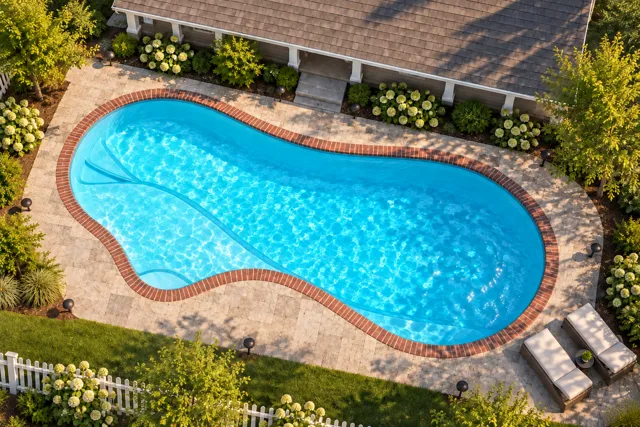 Daytime render of the The Inspiration 35 fiberglass pool with brick coping and a Coral Blue interior, seen from above at an angle.