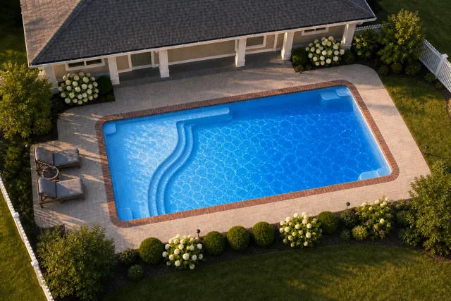 Daytime render of the Aspen 1635 fiberglass pool with brick coping and a California interior, seen from above at an angle.