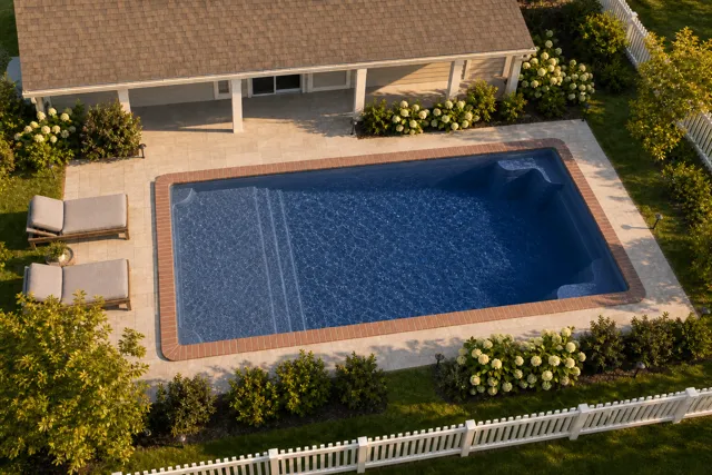 Daytime render of the Corinthian 14 fiberglass pool with brick coping and a Ocean Blue interior, seen from above at an angle.