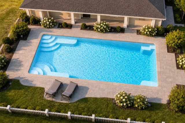 Daytime render of the Goliath 1433 fiberglass pool with stone coping and a Caribbean Sparkle interior, seen from above at an angle.