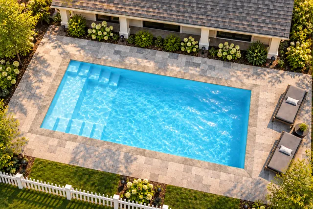 Daytime render of the The Freedom 26 fiberglass pool with stone coping and a Ice Silver interior, seen from above at an angle.