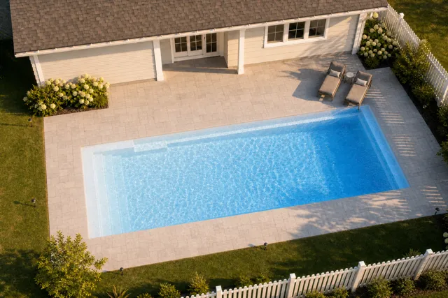 Daytime render of the Claremont fiberglass pool with cantilever coping and a Sapphire Blue interior, seen from above at an angle.