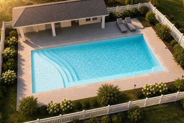 Daytime render of the The Bliss 26 fiberglass pool with stone coping and a Ice Silver interior, seen from above at an angle.