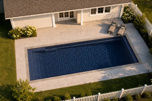 Daytime render of the Claremont fiberglass pool with stone coping and a Night Sky interior, seen from above at an angle.