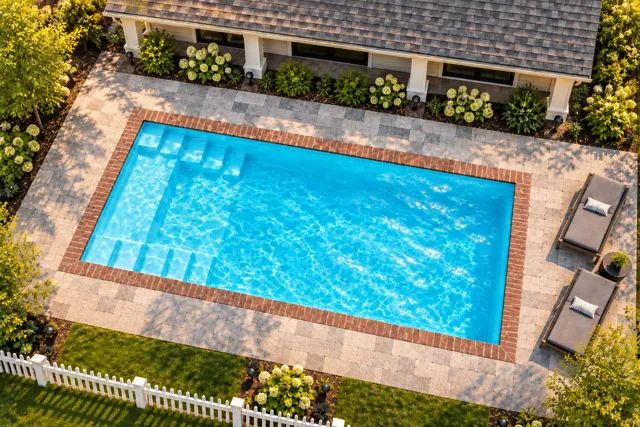Daytime render of the The Freedom 26 fiberglass pool with brick coping and a Coral Blue interior, seen from above at an angle.