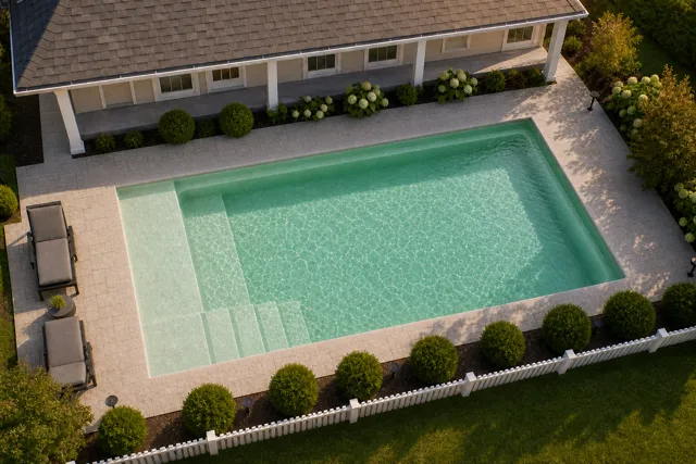 Daytime render of the The Vision 16 fiberglass pool with cantilever coping and a Beach Sand interior, seen from above at an angle.