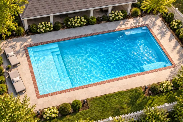 Daytime render of the The Illusion 35 fiberglass pool with brick coping and a Coral Blue interior, seen from above at an angle.