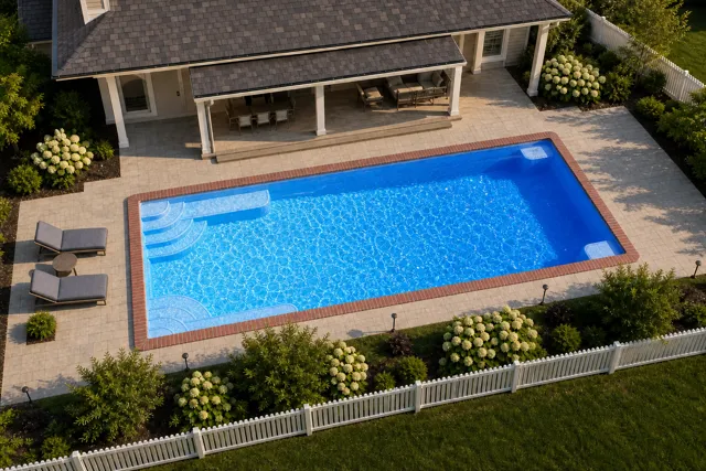 Daytime render of the Goliath 1637 fiberglass pool with brick coping and a California interior, seen from above at an angle.