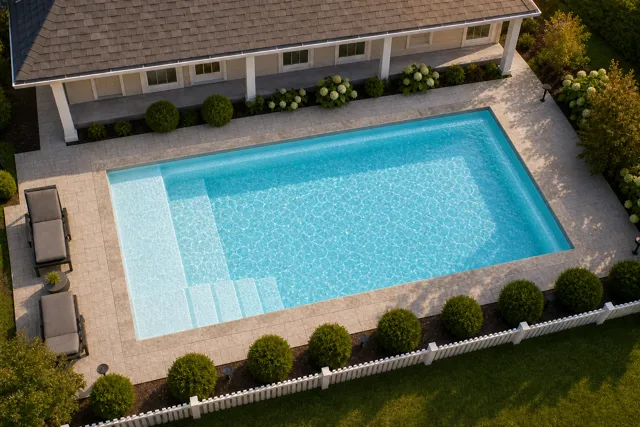 Daytime render of the The Vision 16 fiberglass pool with stone coping and a Ice Silver interior, seen from above at an angle.