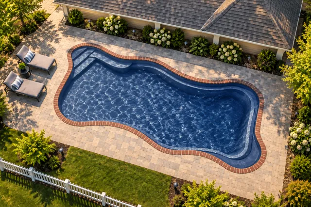 Daytime render of the Cape Cod 16 fiberglass pool with brick coping and a Ocean Blue interior, seen from above at an angle.