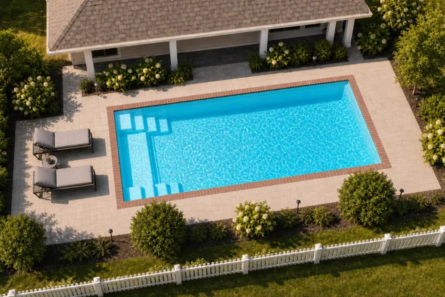 Daytime render of the The Freedom 30 fiberglass pool with brick coping and a Coral Blue interior, seen from above at an angle.