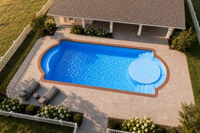 Daytime render of the Cathedral LX 1636 fiberglass pool with brick coping and a California interior, seen from above at an angle.