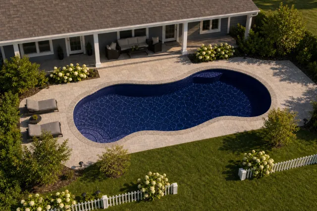 Daytime render of the Bay Isle fiberglass pool with stone coping and a Night Sky interior, seen from above at an angle.