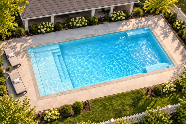 Daytime render of the The Illusion 35 fiberglass pool with stone coping and a Ice Silver interior, seen from above at an angle.