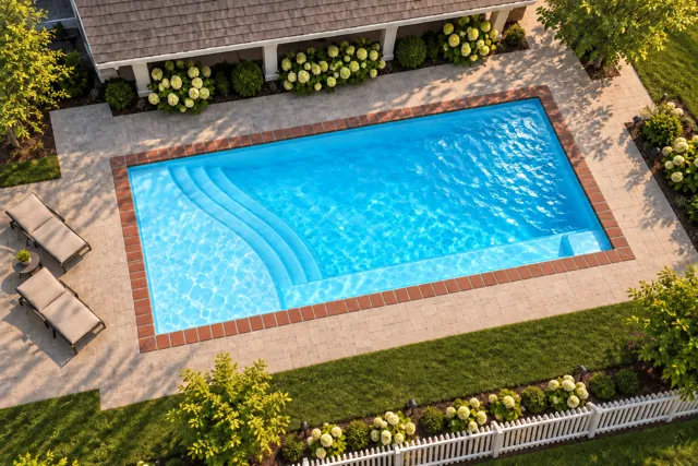 Daytime render of the The Bliss 35 fiberglass pool with brick coping and a Coral Blue interior, seen from above at an angle.