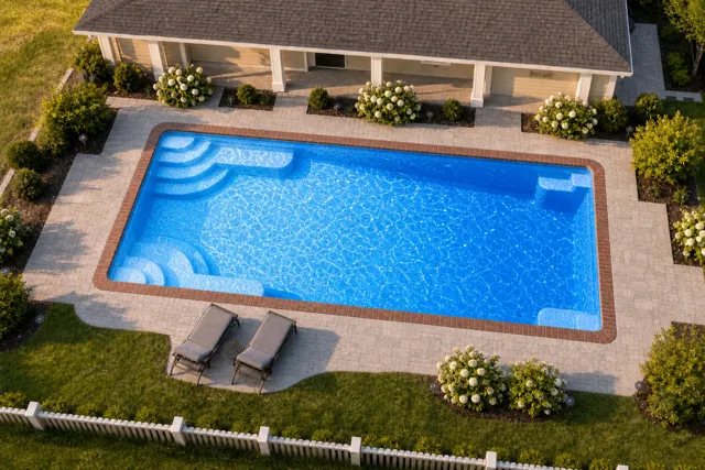 Daytime render of the Goliath 1433 fiberglass pool with brick coping and a California interior, seen from above at an angle.
