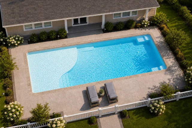 Daytime render of the Grace Beach Entry 1436 fiberglass pool with stone coping and a Caribbean Sparkle interior, seen from above at an angle.