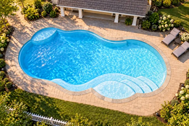 Daytime render of the Sun Day 1530 fiberglass pool with stone coping and a Caribbean Sparkle interior, seen from above at an angle.