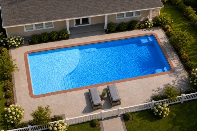 Daytime render of the Grace Beach Entry 1436 fiberglass pool with brick coping and a California interior, seen from above at an angle.