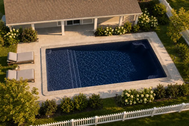 Daytime render of the Corinthian 14 fiberglass pool with stone coping and a Night Sky interior, seen from above at an angle.