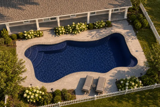 Daytime render of the Cape Cod 12 fiberglass pool with stone coping and a Night Sky interior, seen from above at an angle.