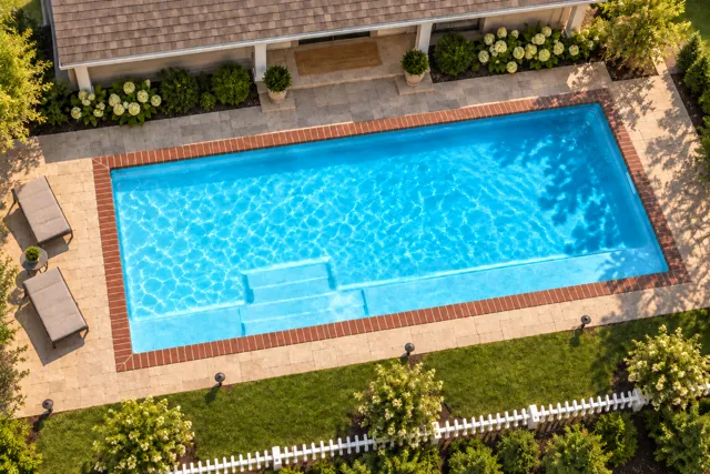 Daytime render of the The Marvelous 35 fiberglass pool with brick coping and a Coral Blue interior, seen from above at an angle.