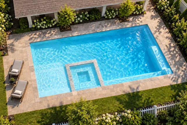 Daytime render of the The Exquisite 30 fiberglass pool with stone coping and a Ice Silver interior, seen from above at an angle.