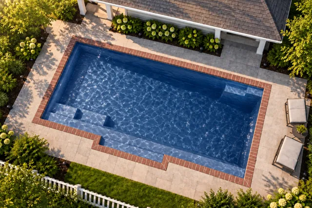 Daytime render of the Tuscan 11.20 fiberglass pool with brick coping and a Ocean Blue interior, seen from above at an angle.