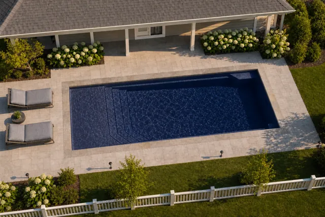 Daytime render of the Apollo 14 fiberglass pool with stone coping and a Night Sky interior, seen from above at an angle.