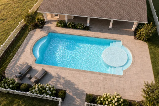 Daytime render of the Cathedral LX 1636 fiberglass pool with stone coping and a Caribbean Sparkle interior, seen from above at an angle.