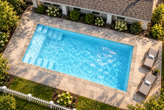 Daytime render of the The Freedom 23 fiberglass pool with stone coping and a Ice Silver interior, seen from above at an angle.