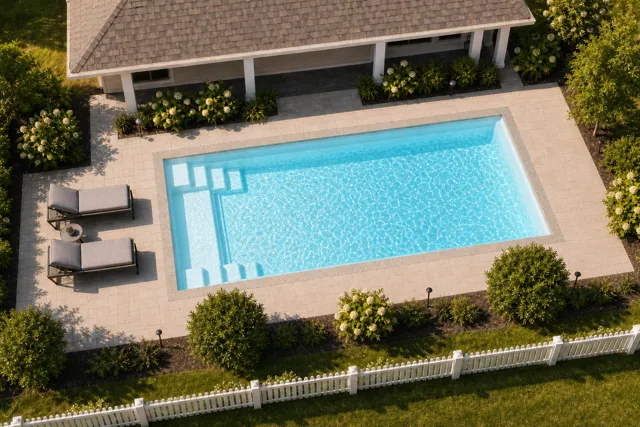 Daytime render of the The Freedom 30 fiberglass pool with stone coping and a Ice Silver interior, seen from above at an angle.