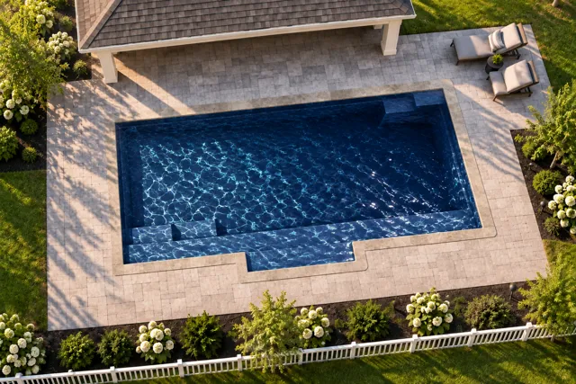 Daytime render of the Tuscan 13.24 fiberglass pool with stone coping and a Night Sky interior, seen from above at an angle.