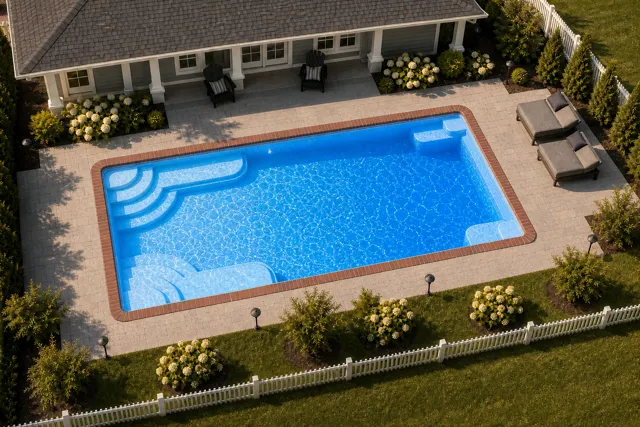 Daytime render of the Goliath 1225 fiberglass pool with brick coping and a California interior, seen from above at an angle.