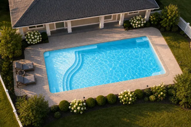 Daytime render of the Aspen 1635 fiberglass pool with stone coping and a Caribbean Sparkle interior, seen from above at an angle.