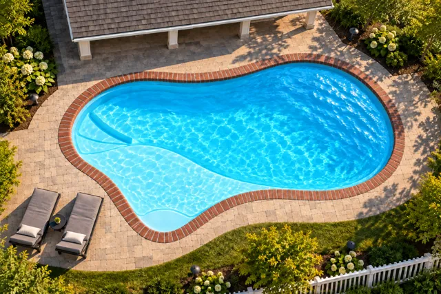 Daytime render of the The Inspiration 23 fiberglass pool with brick coping and a Coral Blue interior, seen from above at an angle.