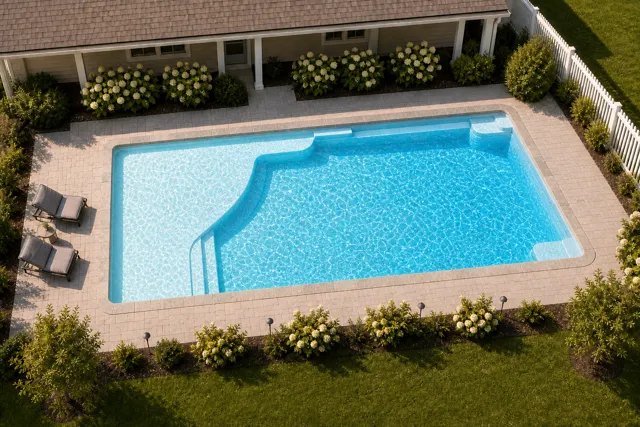 Daytime render of the Grace Beach Entry 1640 fiberglass pool with stone coping and a Caribbean Sparkle interior, seen from above at an angle.