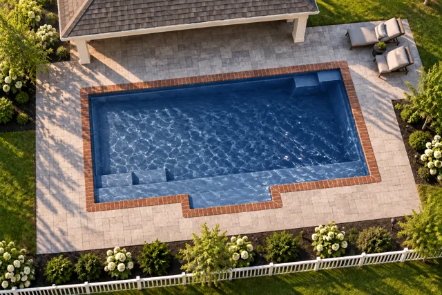 Daytime render of the Tuscan 13.24 fiberglass pool with brick coping and a Ocean Blue interior, seen from above at an angle.