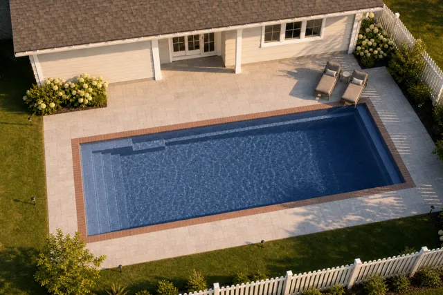 Daytime render of the Claremont fiberglass pool with brick coping and a Ocean Blue interior, seen from above at an angle.