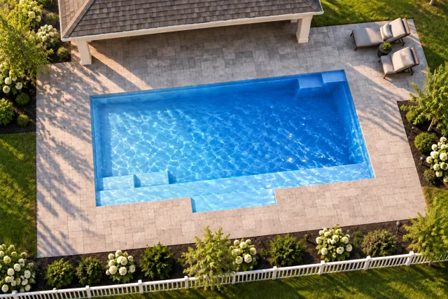 Daytime render of the Tuscan 13.24 fiberglass pool with cantilever coping and a Sapphire Blue interior, seen from above at an angle.